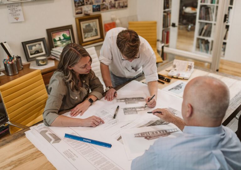Three people collaborating over architectural plans in an office