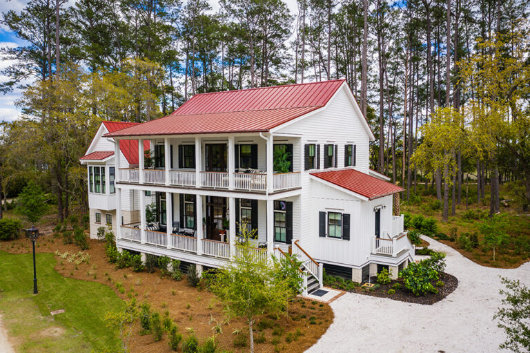 Large Southern-style home with red roof and white exterior, surrounded by trees
