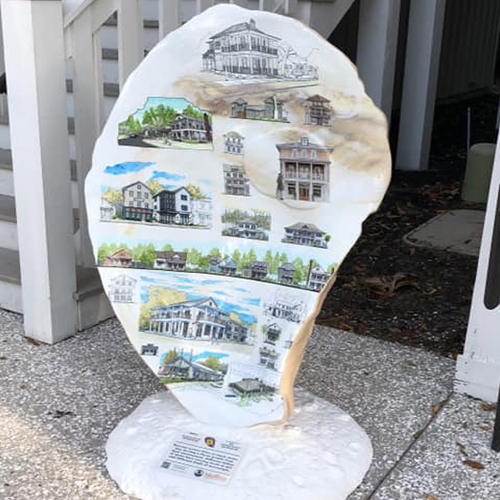 Finished oyster shell art piece with scenic homes painted on surface.