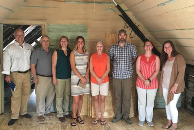 Group of six people standing in a rustic interior during restoration.