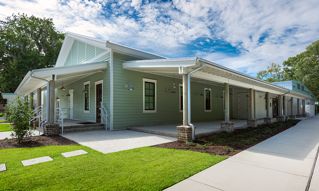 Modern facility with pale green siding and white columns under blue sky.