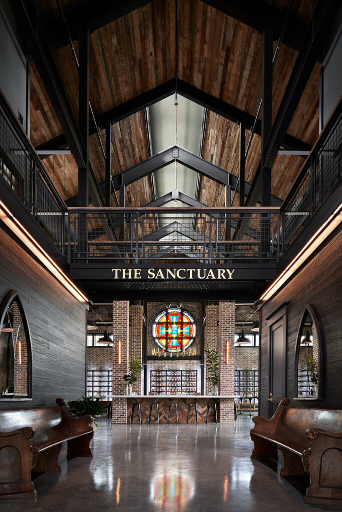 Interior of rustic venue labeled "The Sanctuary" with vaulted wood ceiling and stained glass window.