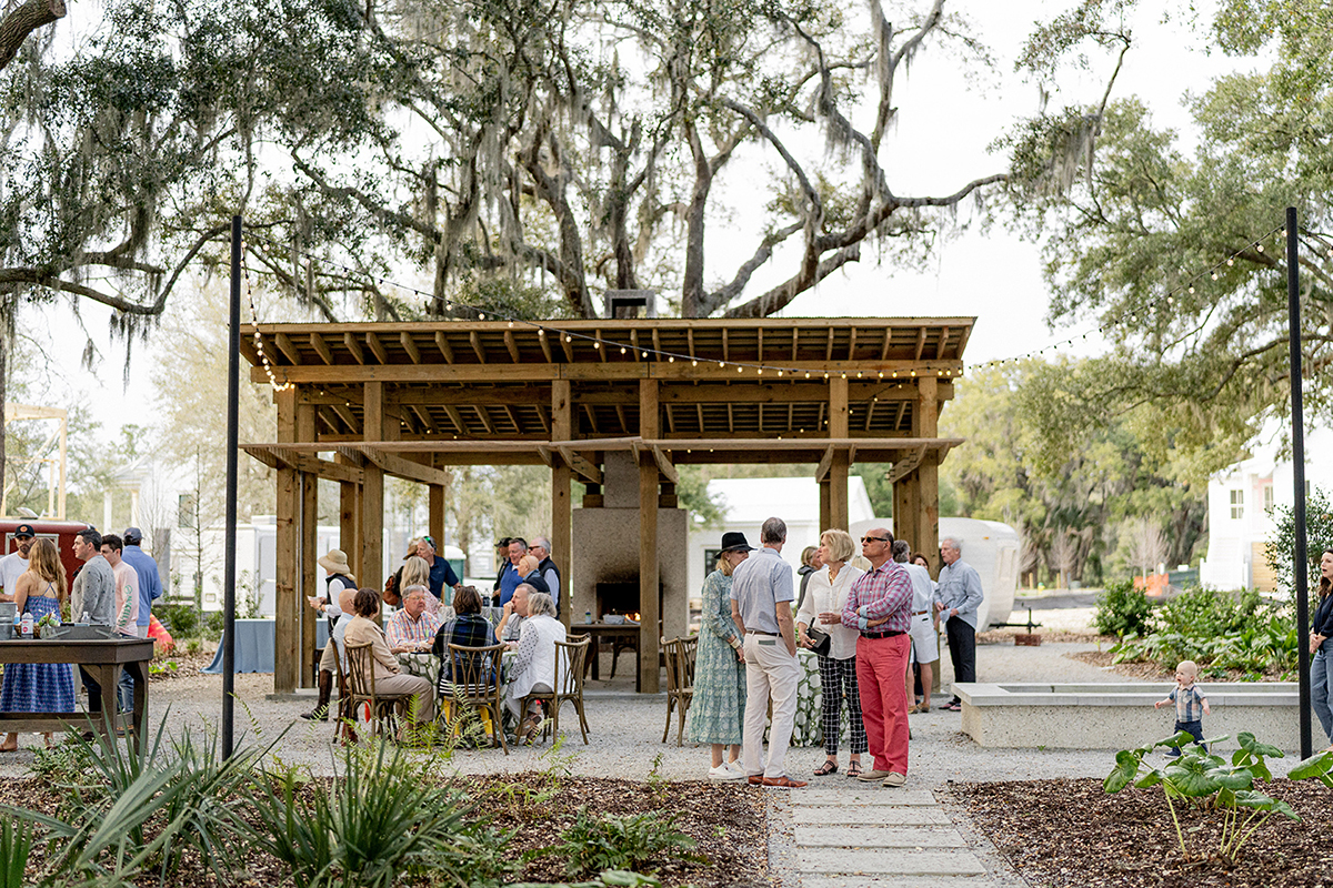 People seated under a rustic wood-beamed shelter in a garden setting.