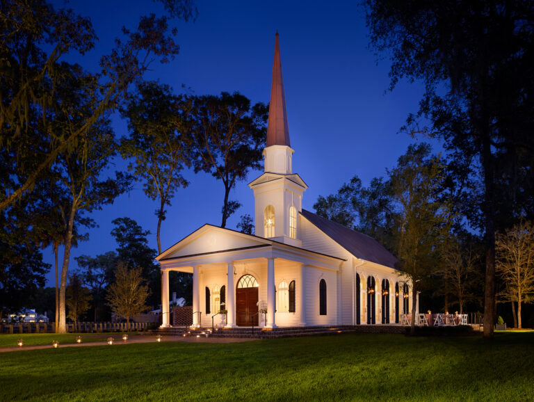 Evening view of chapel with steeple illuminated by exterior lights.