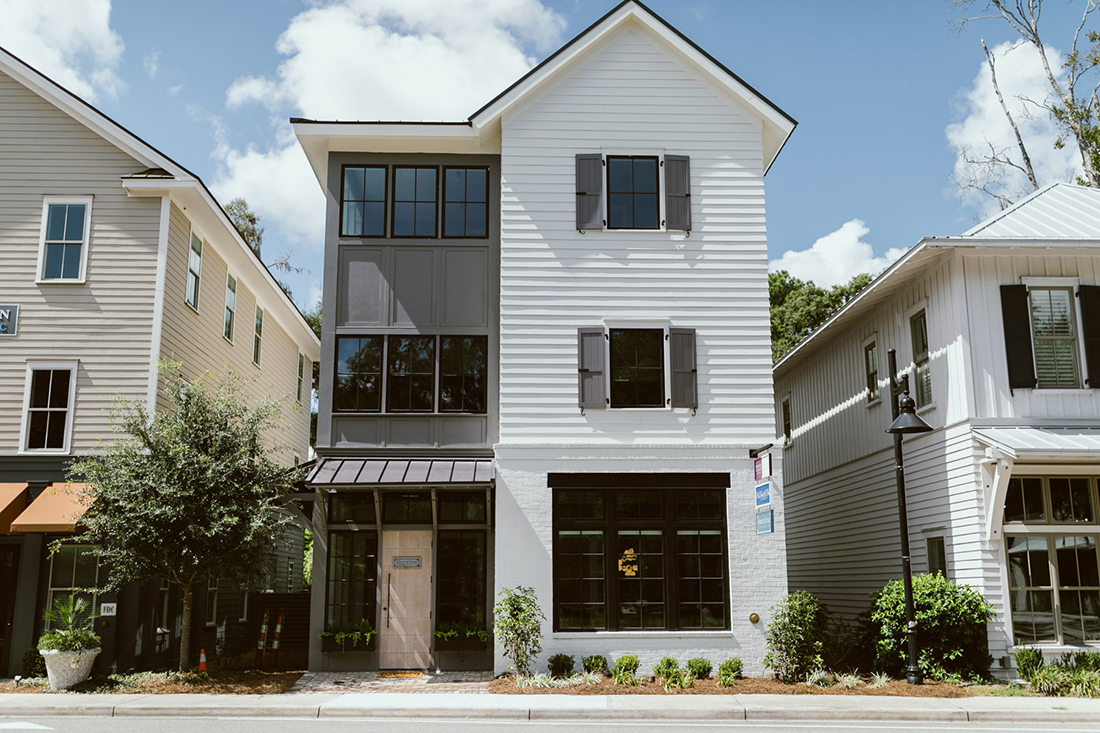 Modern three-story building with light gray siding and black shutters.
