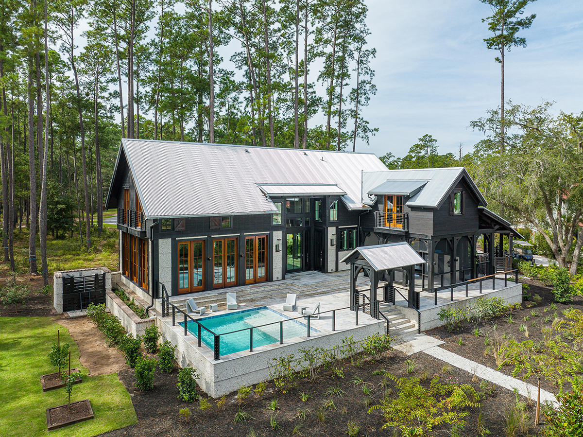 Aerial view of pool, patio, and modern black home with metal roof.