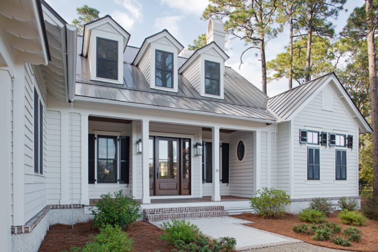 Close-up view of the front entrance of a white modern farmhouse with a covered porch, dormer windows, and black shutters.