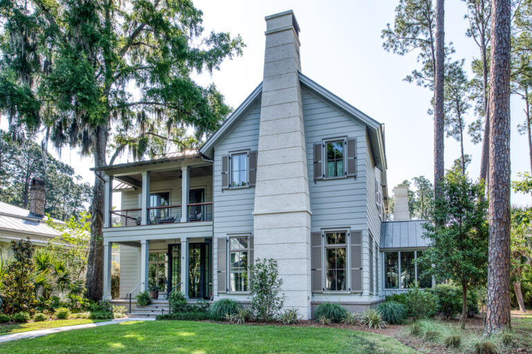 Rear view of shiplap-sided home with large chimney and multiple porches.