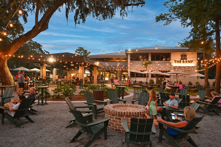 Twilight exterior of a commercial plaza with outdoor seating.